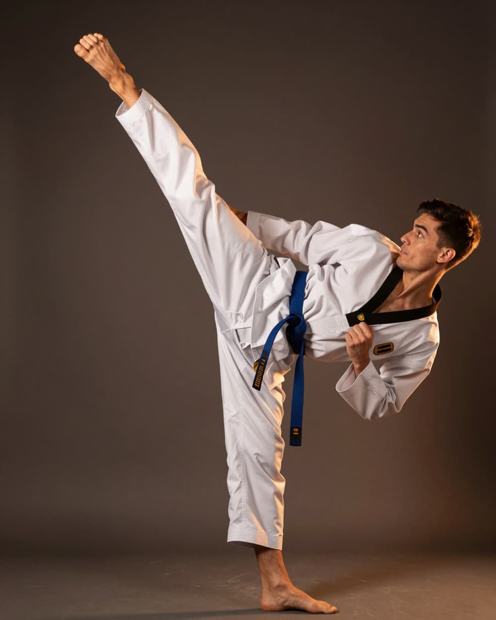 An adult in a blue belt throws a high roundhouse kick